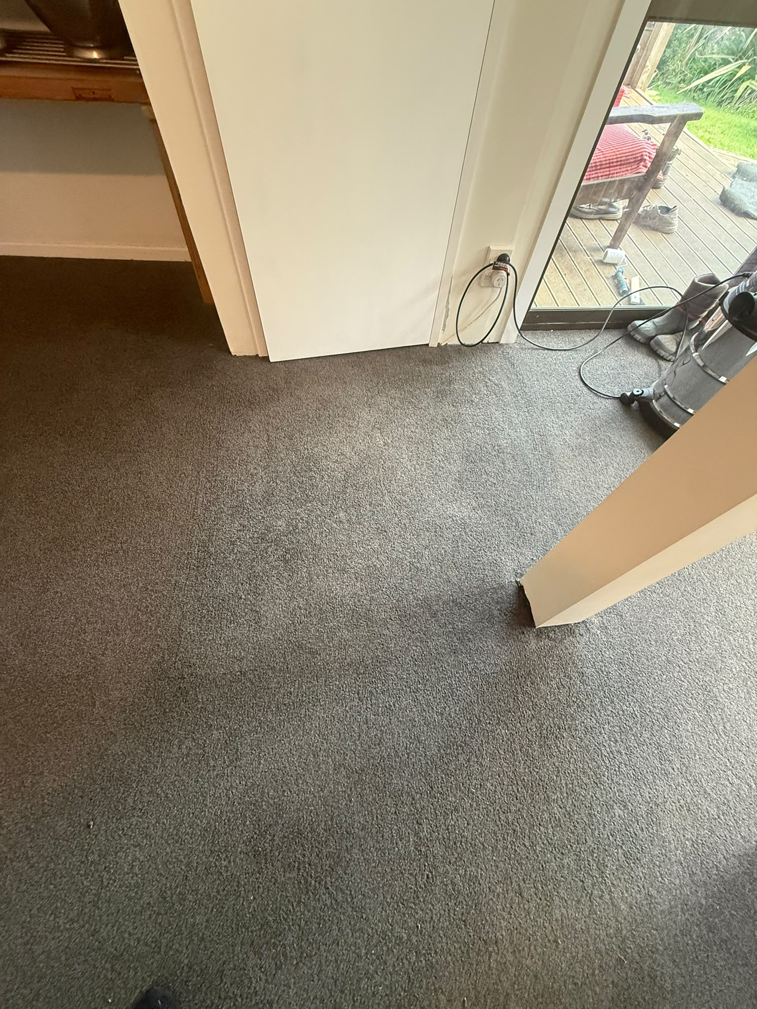 Freshly cleaned grey carpet beside a deck sliding door with cleaning equipment nearby