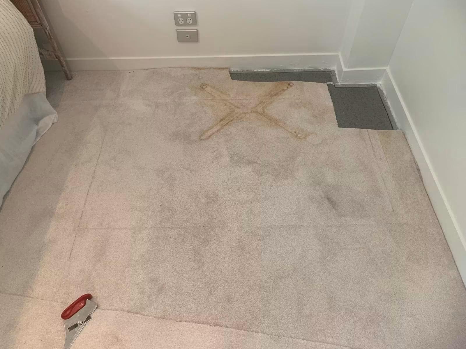 Cream bedroom carpet with a large X-shaped rust stain left by a metal stand