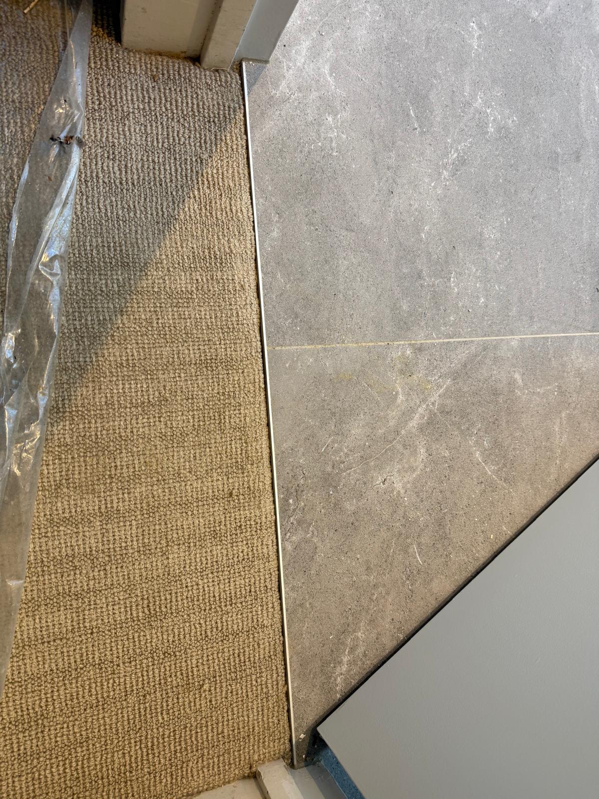 Clean join between tan carpet and grey tile at a doorway threshold with a neat metal trim